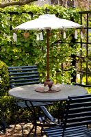 Circular garden table with small parasol and backed by black painted trellis