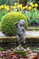 Putto statue in the centre of a circular pond with clipped Buxus ball behind