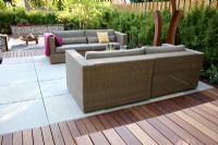 Small garden with wicker sofas on decked and paved patio, backed by Fargesia murielae - Bamboo hedge 