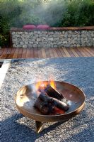 Fire pit on gravel patio in small garden. Gabion bench backed by Fargesia murielae - Bamboo hedge