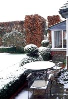 Patio in winter with snow covered furniture, topiary and Fagus - Beech hedge