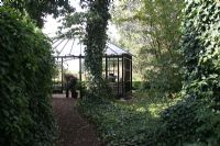 Path through woodland garden with greenhouse at the end. The Netherlands.