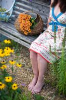 Woman wearing a summer dress, sitting on a garden bench with orange flowers in a vintage basket 