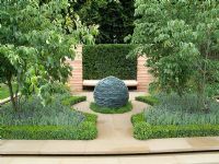 Symmetrical garden with central Lakeland stone sphere, Buxus topiary and Lavandula stoechas 'Anouk'. Wooden bench with Taxus - Yew behind. The Christie 'Embracing Tranquility' garden. RHS Tatton Flower Show 2010