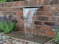 Water falling over brick wall into drain and cobbled surface. The Russell Watkinson Landscapes 'It's a Reflection of Life' garden - RHS Tatton Flower Show 2010