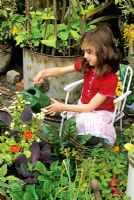 Young girl sitting in a chair, watering her own small scale kitchen garden