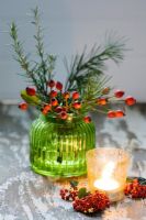 Christmas decoration of rosehips, rosemary, fir tree foliage and Cotoneaster berries in a green glass vase
