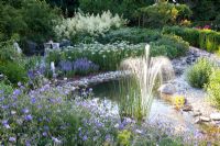 Pond with fountain, planting of Persicaria polymorpha, Achillea, Alchemilla mollis and Geranium 'Spinners' 