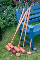 Croquet mallets leaning against a blue bench on a lawn