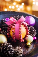 Making a Cranberry and Orange pomander for Christmas - finished pomander in a dark wood bowl with pine cones and baubles