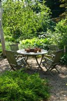 Wooden table and chairs in front woodland garden, June. Sandhill Farm House, Hampshire.