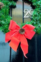 Wreath with red ribbon bow and pine cone, hanging on black door