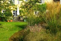 Central circular bed is a mass of graceful grasses and herbaceous perennials including Miscanthus 'Morning Light', Stipa gigantea, Calamagrostis x acutiflora 'Karl Foerster', Allium pulchellum and bronze fennel with house behind - Grass Garden, Hants