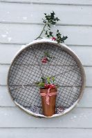 Snowy rusty pot with Ilex - Holly sprigs balanced on wooden sieve
