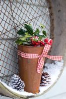 Snowy rusty pot with Ilex - Holly sprigs balanced on wooden sieve
