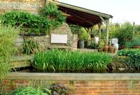 Wooden Loggia and pond with Iris foliage in late Spring. Fovant Hut Garden, Wilts