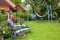 Family country garden with childrens play equipment and loungers on lawn
