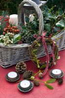 Christmas basket of natural folilage of holly, rosehips, ivy berries, pine cones, Viburnum with rustic wreath, mistletoe and candles