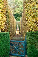 Blue gate leading to clipped Fagus and Taxus baccata hedges and stone obelisk - Silverstone Farm, Norfolk
