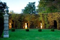 Clipped Fagus hedging, arches with stone urns on plinths with uplighters, clipped box balls on lawn - Silverstone Farm, Norfolk