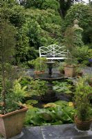 Formal garden with pool, fountain, white painted seat, containers and water lilies - The Lost Gardens of Heligan