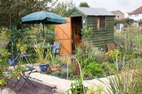 Small shed on allotment with gravel path, mixed planting and seating area