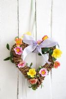 Heart shaped wreath decorated with pink, yellow and orange primrose flowers and periwinkle foliage