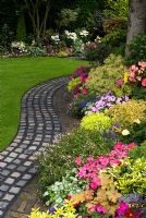Reclaimed cobbles and bricks used to make curving path by lawn and raised border with mixed rich late summer planting including Parahebe, Begonia, Impatiens, Euonymus, Lamium, Lobelia and Heuchera. Brocklebank Road, Southport, Lancashire NGS