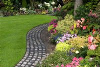 Reclaimed cobbles and bricks used to make curving path by lawn and raised border with mixed rich late summer planting including Parahebe, Pieris, Begonia, Impatiens and Lobelia. Brocklebank Road, Southport, Lancashire NGS