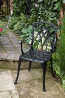 Cast iron decorative chair on stone slab patio, Hosta and Hedera behind - Brocklebank Road, Southport, Lancashire NGS