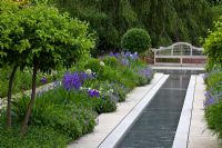 Perennial bed with Geranium pratense 'Johnson's Blue' and Iris sibirica edging a water rill that leads to a wooden bench