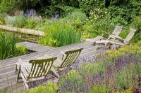 Oak deck by natural swimming pool with reclining chairs. Buxus sempervirens balls in raised oak bed planted with Lavandula and Heauchera.
