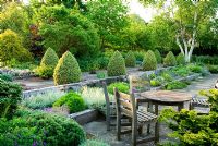 Seating area with raised beds made wit weathered railway sleepers. Two lines of Buxus sempervirens 'Elegantissima' clipped into cones frame a path of slabs set into gravel with Betula platyphylla beyond - Ivy Croft, Leominster, Herefordshire, UK
