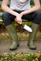 Man in wellies sitting on a garden bench holding a stainless steel trowel