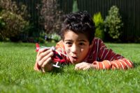 Boy relaxing on the lawn playing with a toy helicopter