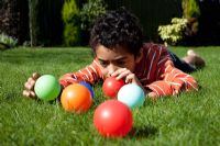 Boy lying down on grass playing with brightly coloured balls