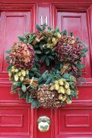 Christmas wreath made of conifer greenery and decorated with dried Hydrangea flowers, hops, cinnamon sticks, pine cones and coils of string on a red Georgian door