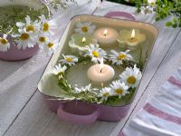 Small wreath of Leucanthemum and herbs with little white candles in glass lined baking dish