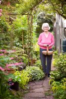Mary Eastwood holding a trug and secateurs in her garden - 35 heyes Lane