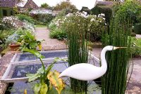 Heron by Michael Lythgoe guarding a pond at the centre of the White Garden beside Equisetum hyemale - Horsetail.  Bourton House, Bourton-on-the-Hill, Moreton-in-Marsh, Glos, UK