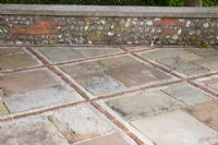 Paving of old slabs with bricks and walling of flint and brick. West Dean Gardens