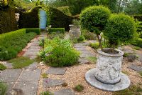 The Secret Herb Garden, with Privet in Urn and Thyme growing between stone slabs, Yew hedge and face sculpture - Tilford Cottage, Surrey 
