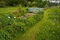 The bog garden, with Monet style bridge and sculpture of silver balls rolling into water, planted with Irises, wildflower meadow and mown path - Tilford Cottage, Surrey