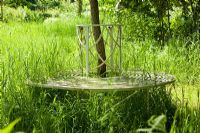 White ironwork circular tree seat in a wildflower meadow.