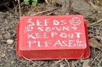 Red upturned cat litter tray with seeds sown keep out please written on the back