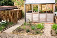 Wooden greenhouse with adjacent gravel paths and beds in kitchen garden at 'The Croft', Flore, Northamptonshire. The garden is open for The National Garden Scheme