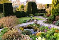 A sheltered terrace around the house is protected by yew hedges shaped like ramparts. Shrubs include Prunus incisa, variegated box, hellebores, acers and hebes with delicate narcissi and primulas in containers and by a small pond. Chiffchaffs, nr Bourton, Dorset, UK