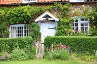 Small flint country cottage with climbing Rosa and cottage garden flowers, Norfolk, England, June