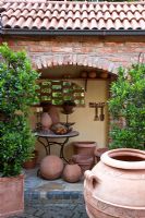 Patio and gangway with bistro table, terracotta urns, objects and containers planted with Laurus nobilis