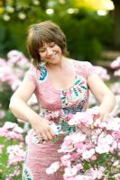 Woman in a pink dress deadheading or cutting roses with secateurs